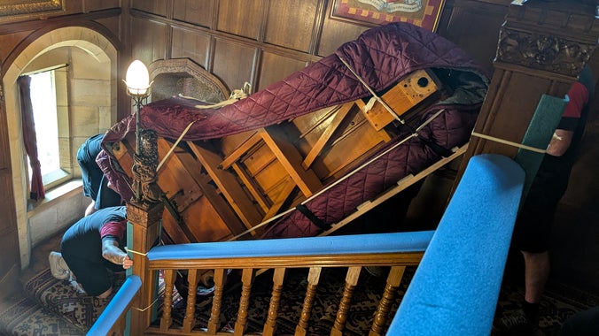 The Broadwood Piano being brought up the stairs by a team of piano movers.